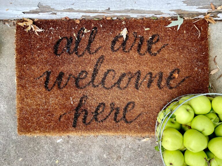 "All are welcome here" written on a mat